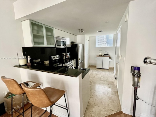 kitchen featuring appliances with stainless steel finishes, white cabinetry, a breakfast bar area, and kitchen peninsula