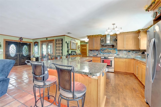 kitchen featuring wall chimney range hood, decorative backsplash, a kitchen breakfast bar, light wood-type flooring, and stainless steel appliances