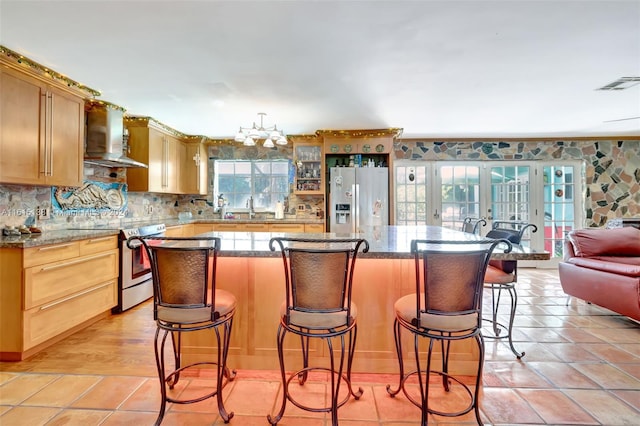 kitchen featuring wall chimney range hood, stainless steel appliances, a kitchen bar, and a kitchen island