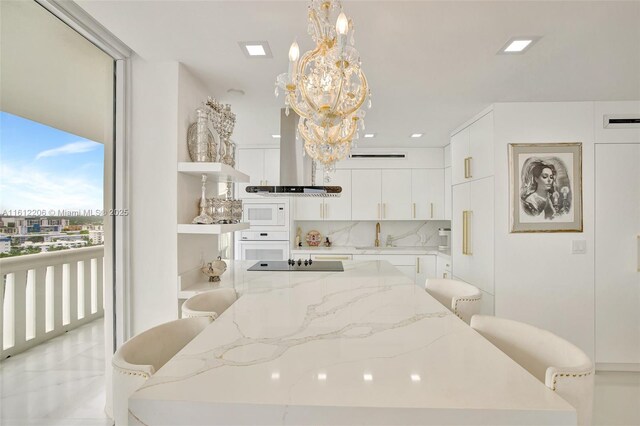 kitchen featuring island range hood, pendant lighting, white cabinets, a kitchen bar, and white appliances