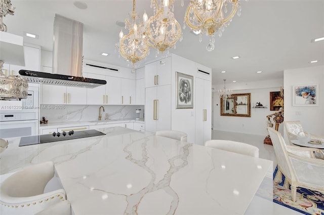 kitchen featuring a chandelier, island range hood, white cabinets, white oven, and pendant lighting