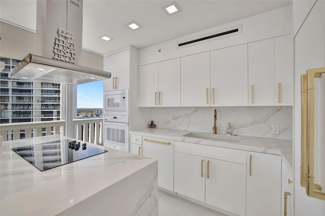 kitchen with white appliances, island range hood, white cabinets, light stone counters, and a sink