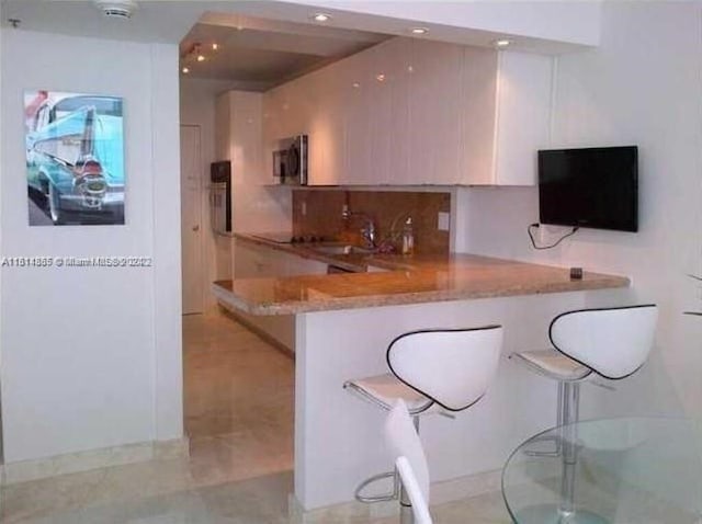 kitchen with a breakfast bar, sink, decorative backsplash, light stone counters, and kitchen peninsula