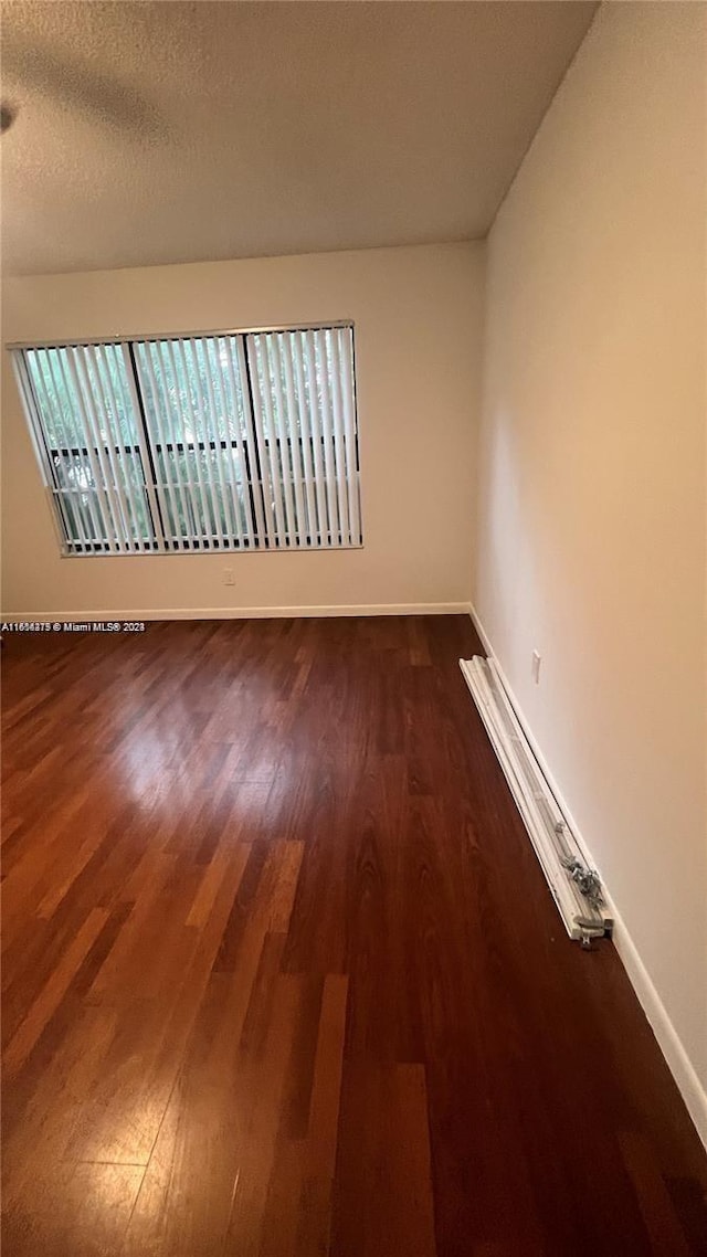 unfurnished room featuring dark wood-type flooring and a textured ceiling