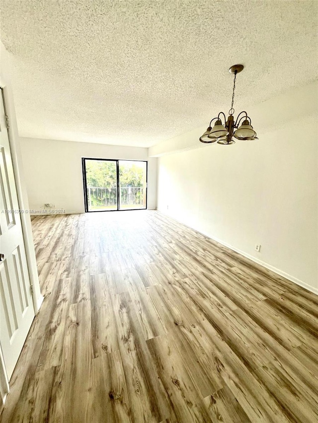 unfurnished living room with a textured ceiling, wood-type flooring, and an inviting chandelier