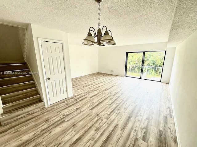 unfurnished dining area with an inviting chandelier, light hardwood / wood-style flooring, and a textured ceiling