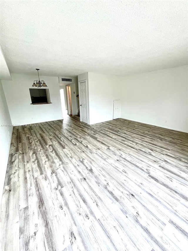 unfurnished living room with a notable chandelier, a textured ceiling, and light wood-type flooring