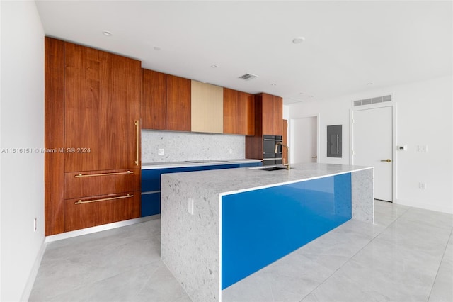 kitchen with sink, tasteful backsplash, electric panel, a center island with sink, and black appliances