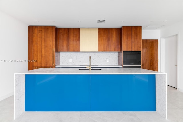 kitchen with sink, tasteful backsplash, double oven, and an island with sink