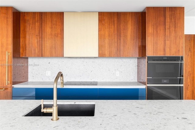 kitchen with decorative backsplash, light stone countertops, black double oven, and sink