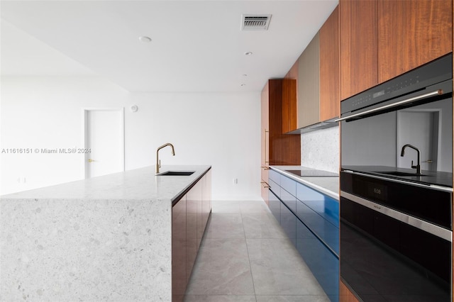 kitchen featuring black appliances, sink, light tile patterned floors, and a kitchen island with sink