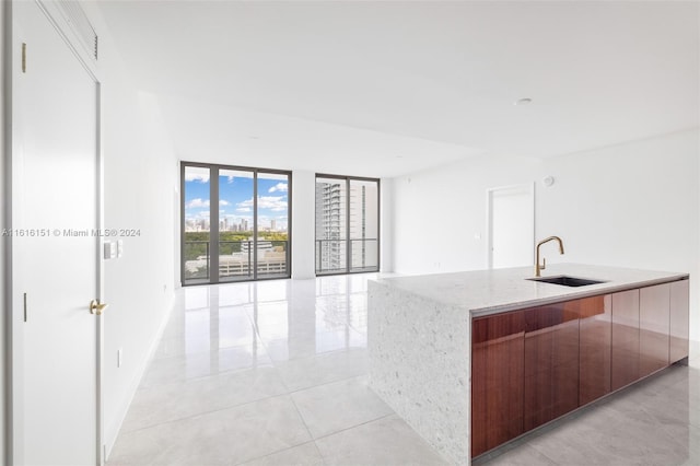 kitchen with light tile patterned flooring, light stone countertops, a spacious island, and sink