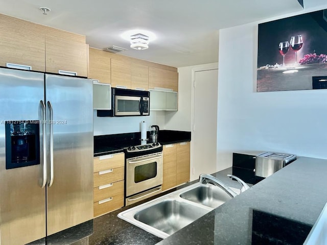 kitchen with light brown cabinets, sink, stainless steel appliances, and dark stone counters