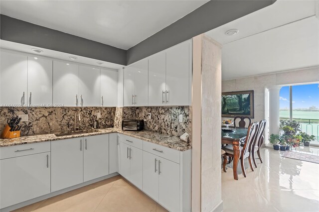 kitchen with tasteful backsplash, white cabinets, sink, light stone countertops, and light tile patterned flooring