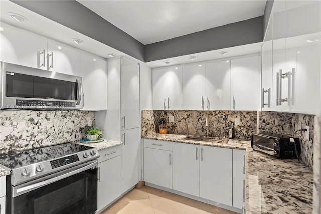 kitchen featuring light tile patterned flooring, appliances with stainless steel finishes, white cabinetry, sink, and light stone countertops