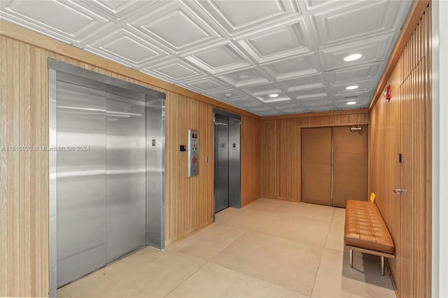 hallway featuring elevator, wooden walls, and light tile patterned floors