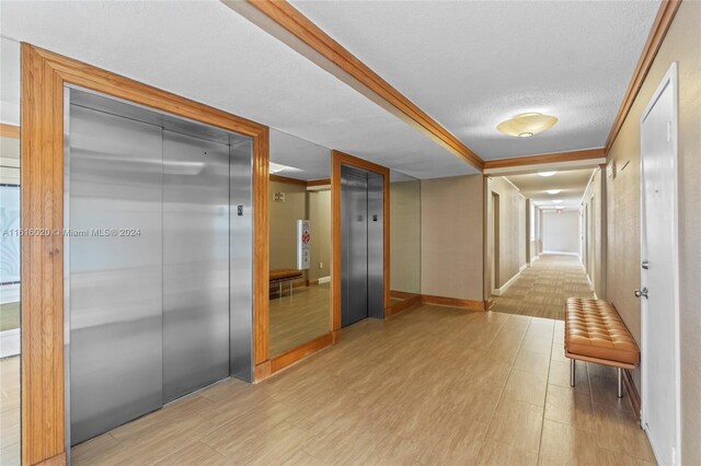 corridor with light hardwood / wood-style flooring, elevator, and a textured ceiling