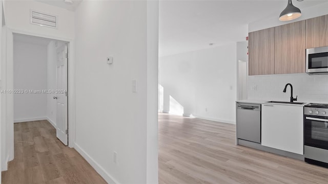 kitchen with sink, appliances with stainless steel finishes, light wood-type flooring, pendant lighting, and decorative backsplash