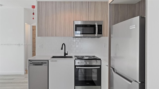 kitchen with stainless steel appliances, sink, tasteful backsplash, light brown cabinets, and light wood-type flooring