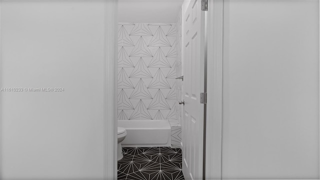 bathroom featuring tile patterned flooring, toilet, and tiled shower / bath combo