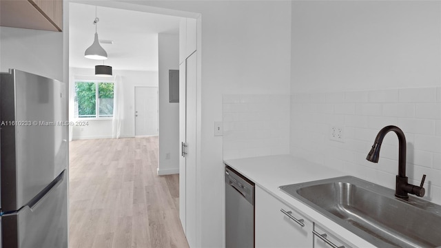 kitchen featuring light wood-type flooring, appliances with stainless steel finishes, decorative light fixtures, sink, and white cabinets