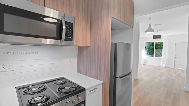 kitchen featuring stainless steel appliances, hanging light fixtures, tasteful backsplash, and light hardwood / wood-style flooring