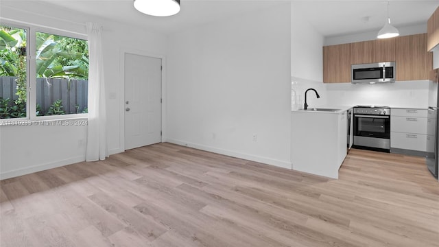 kitchen featuring stainless steel appliances, light hardwood / wood-style floors, sink, decorative light fixtures, and decorative backsplash