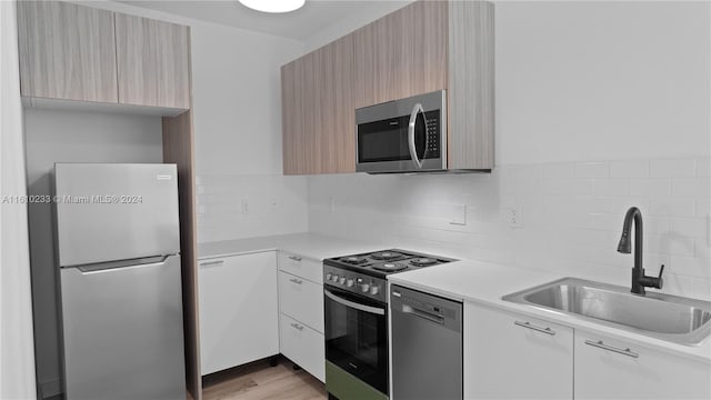 kitchen featuring backsplash, appliances with stainless steel finishes, sink, and light hardwood / wood-style flooring