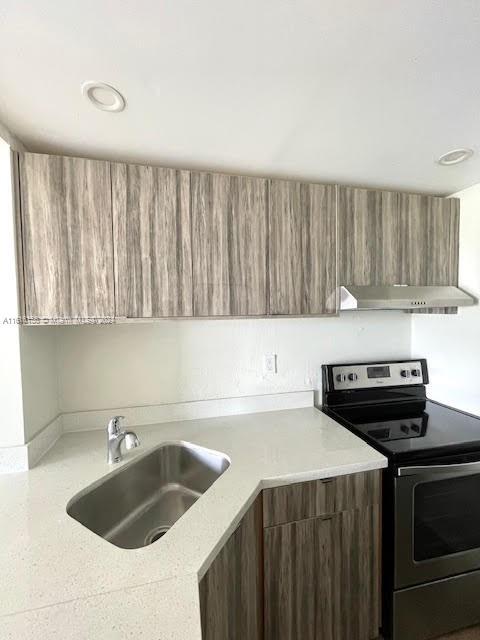 kitchen with light stone counters, electric stove, sink, and range hood