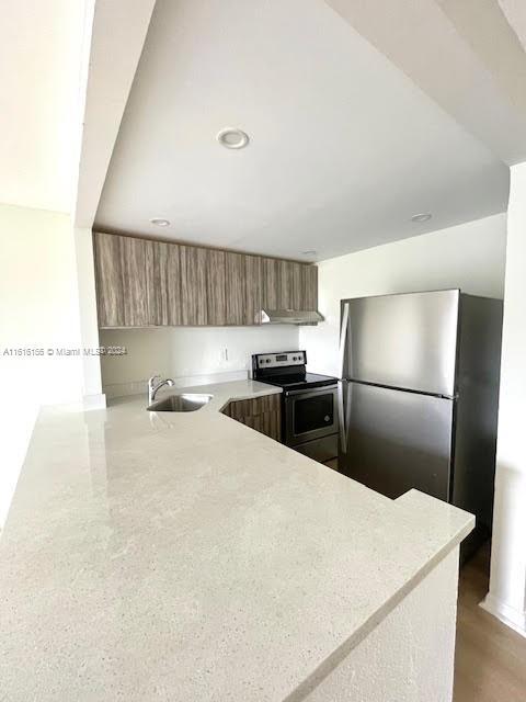 kitchen with kitchen peninsula, sink, exhaust hood, and appliances with stainless steel finishes