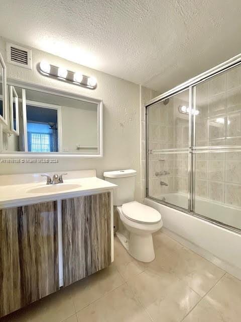 full bathroom featuring tile patterned floors, bath / shower combo with glass door, a textured ceiling, toilet, and vanity