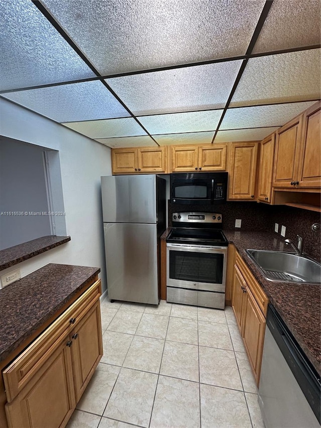 kitchen featuring appliances with stainless steel finishes, backsplash, sink, dark stone countertops, and light tile patterned flooring