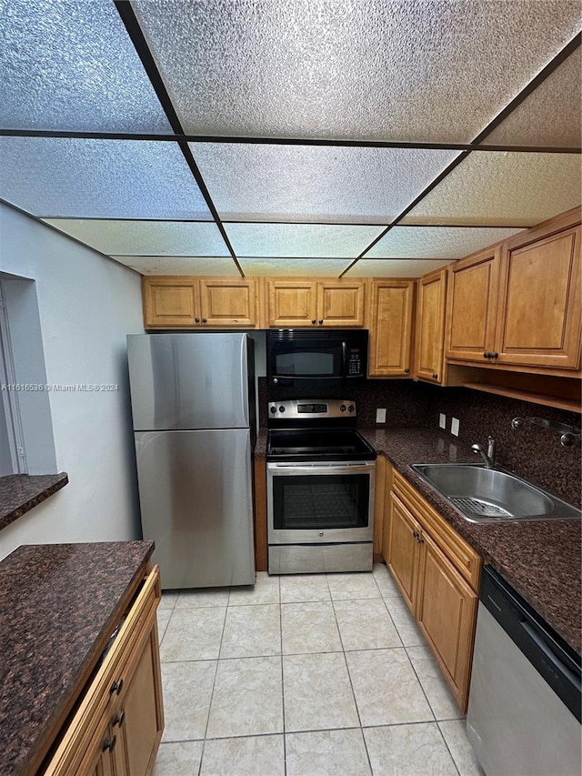 kitchen with sink, a drop ceiling, stainless steel appliances, dark stone countertops, and light tile patterned flooring