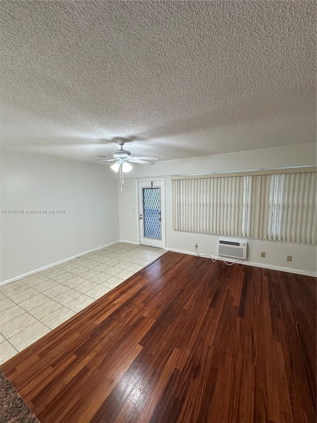 empty room with ceiling fan, light wood-type flooring, a textured ceiling, and an AC wall unit