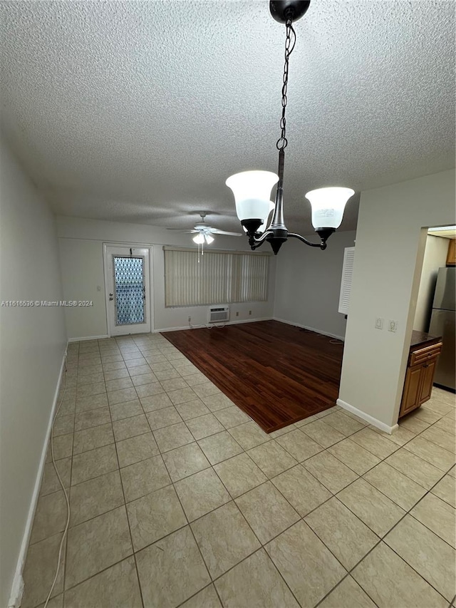 unfurnished dining area with a wall mounted air conditioner, ceiling fan with notable chandelier, light hardwood / wood-style floors, and a textured ceiling