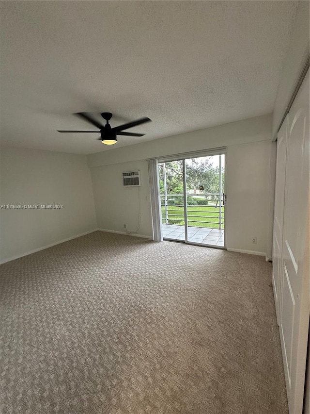 carpeted spare room with a wall unit AC, ceiling fan, and a textured ceiling