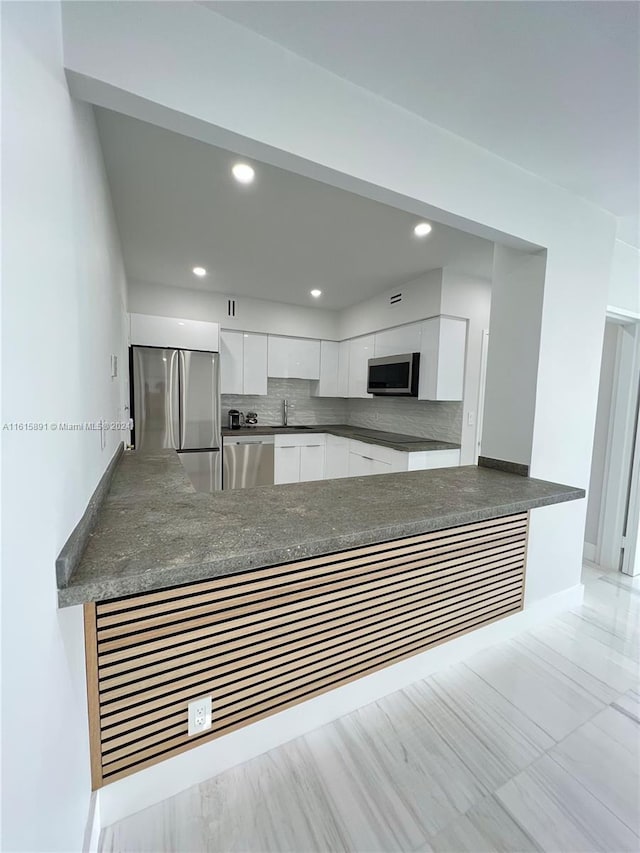 kitchen with tasteful backsplash, kitchen peninsula, white cabinets, and appliances with stainless steel finishes