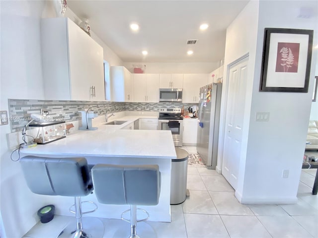 kitchen featuring stainless steel appliances, kitchen peninsula, decorative backsplash, light tile patterned flooring, and white cabinetry