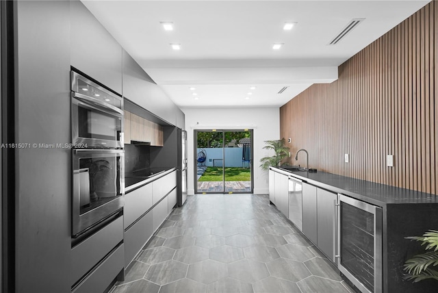 kitchen with sink, beverage cooler, appliances with stainless steel finishes, and wooden walls