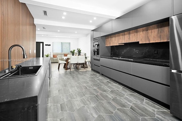 kitchen featuring decorative backsplash, dark stone counters, sink, and stainless steel refrigerator