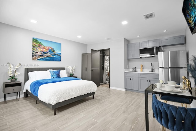 bedroom with light wood-type flooring, connected bathroom, sink, and stainless steel fridge