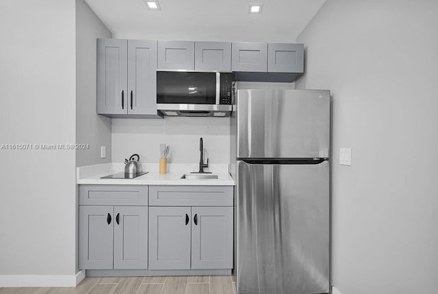 kitchen with gray cabinets, stainless steel appliances, sink, and light hardwood / wood-style flooring