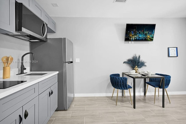 kitchen featuring gray cabinets, light stone countertops, appliances with stainless steel finishes, and sink