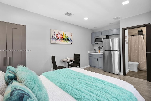 bedroom featuring stainless steel fridge, ensuite bath, sink, and light hardwood / wood-style flooring