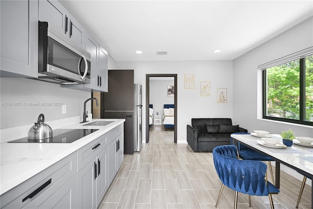 kitchen featuring black electric cooktop, light stone counters, sink, gray cabinetry, and light hardwood / wood-style flooring