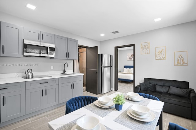 kitchen with gray cabinets, light wood-type flooring, appliances with stainless steel finishes, and sink