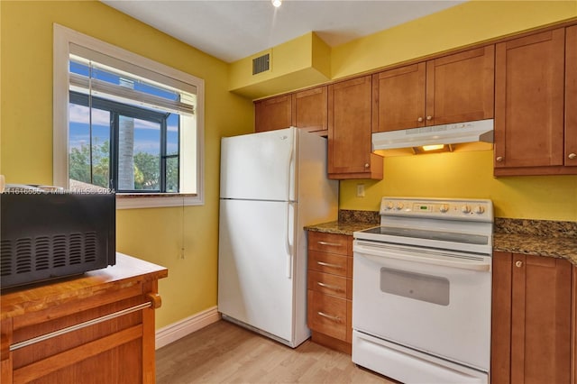 kitchen with dark stone counters, light wood-type flooring, and white appliances