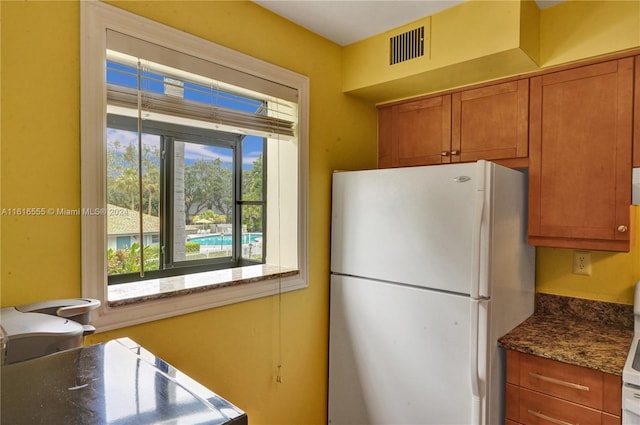 kitchen featuring brown cabinetry, visible vents, dark stone countertops, and freestanding refrigerator