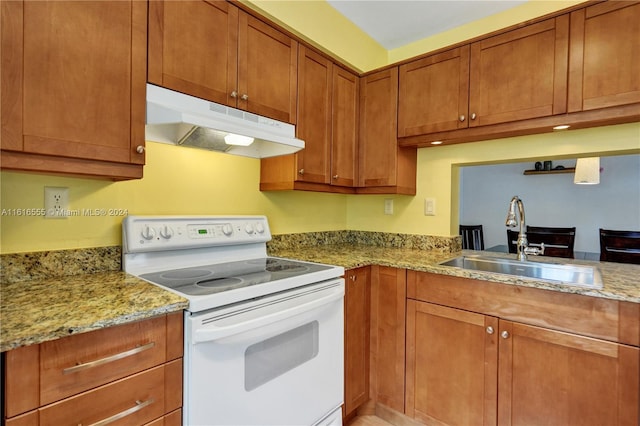 kitchen with light stone countertops, brown cabinetry, white range with electric cooktop, a sink, and under cabinet range hood