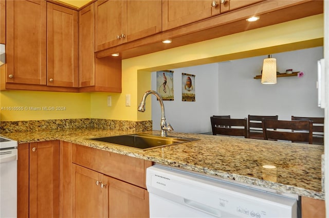 kitchen with light stone countertops, brown cabinets, white dishwasher, stove, and a sink